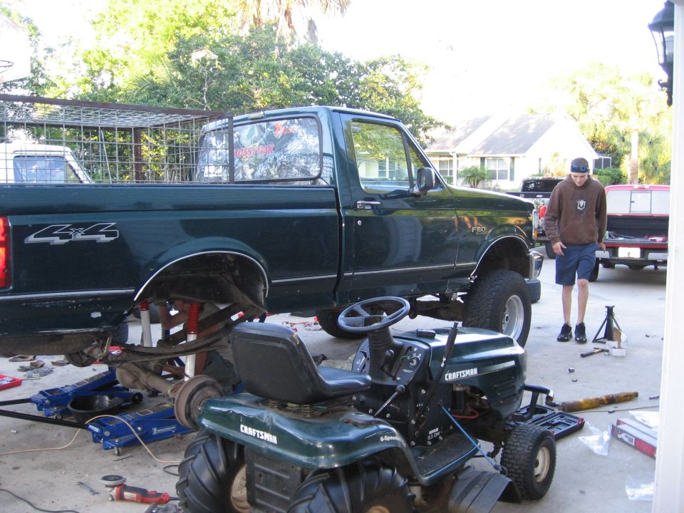 Side view of dark green pickup truck with "4x4" badge, lifted for repairs