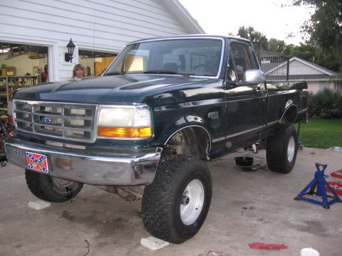 1974 Ford F-100 - Green Ford F-150 pickup truck is lifted on blocks in a driveway, undergoing maintenance.
