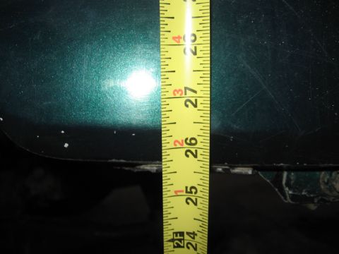 1974 Ford F-100 - A yellow measuring tape is placed against a green metallic car body panel, indicating a measurement.