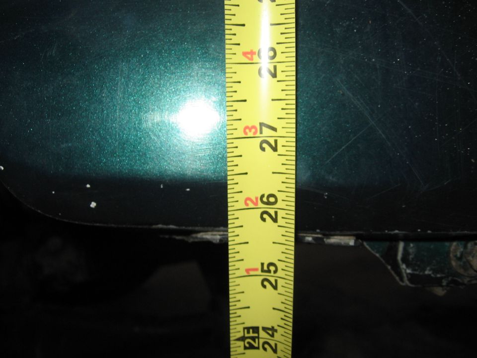 Green metallic car body panel with a yellow measuring tape showing approximately 25.5 inches