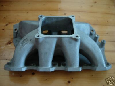 1972 Ford Ranchero - Aluminum intake manifold with a square opening for a carburetor sits on a wooden surface.