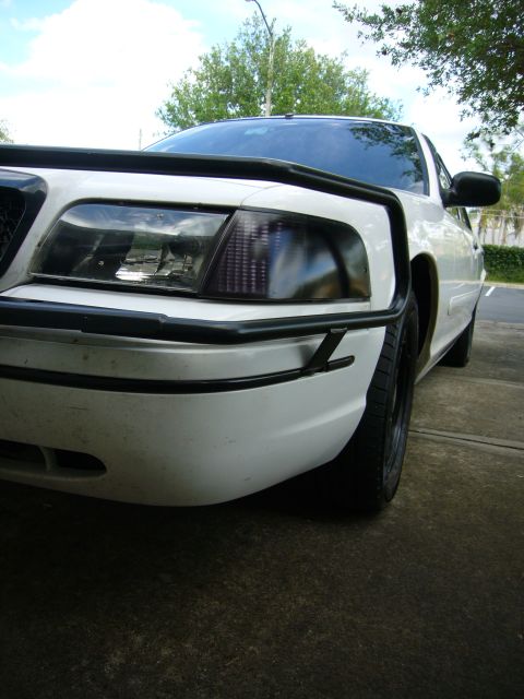 2000 Ford Crown Victoria - The front end of a white sedan is visible, a black push bumper and tinted headlights.