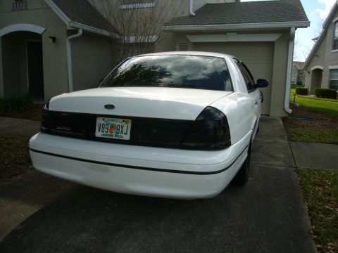2000 Ford Crown Victoria - Rear three-quarter view of a white Ford full-size sedan parked in a residential driveway, with blacked-out/smoked tail light lenses, dark t…