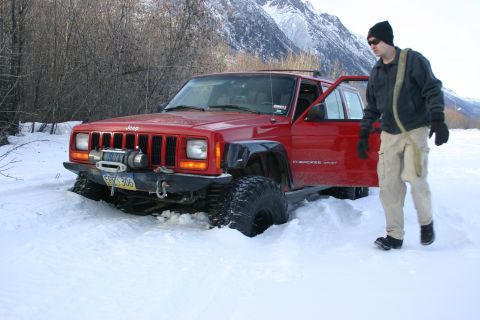 2003 Jeep TJ - A red Jeep Cherokee XJ is stuck in deep snow with a person exiting the vehicle.