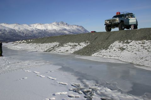 2003 Jeep TJ - A light blue SUV is parked on a gravel ridge with a frozen body of water in the foreground and snow-covered mountains in the background.