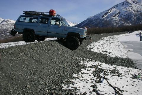 2003 Jeep TJ - Blue SUV parked on a gravel slope with a snowy mountain landscape and frozen water in the background.
