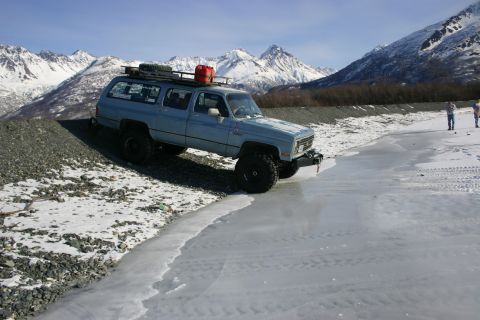 2003 Jeep TJ - A light blue SUV navigates a frozen landscape with snow-capped mountains under a clear sky.
