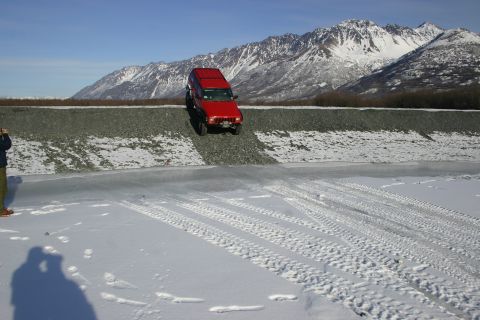 2003 Jeep TJ - Red Jeep Cherokee navigates a snowy embankment with tire tracks visible in the foreground.