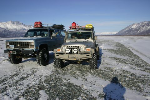 2003 Jeep TJ - Two modified SUVs, a Chevrolet Blazer and a Jeep Wrangler, are parked side-by-side in a vast, snow-covered, mountainous area.