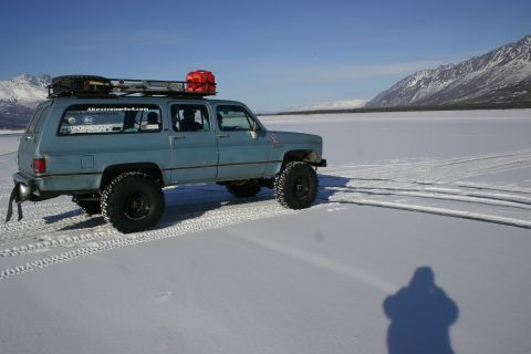 2003 Jeep TJ - A blue SUV equipped with a roof rack and a red gas can is parked on a vast, snow-covered plain with mountains in the background.