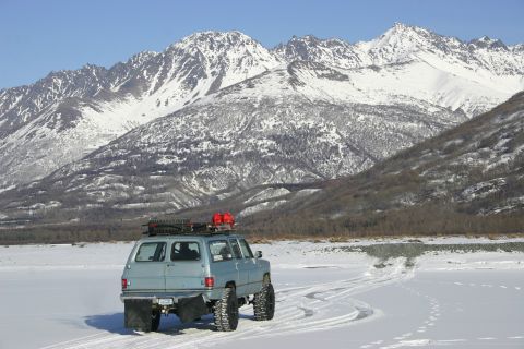2003 Jeep TJ - An SUV equipped for off-road conditions drives through a snowy landscape with mountains in the distance.