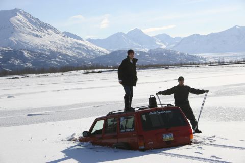 2003 Jeep TJ - Jeep Cherokee stuck in snow with two people nearby, mountains in the distance.