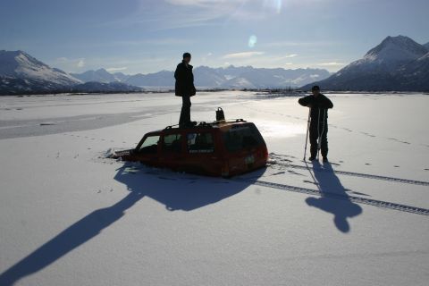 2003 Jeep TJ - A red SUV is stuck in the snow with two people standing around it.