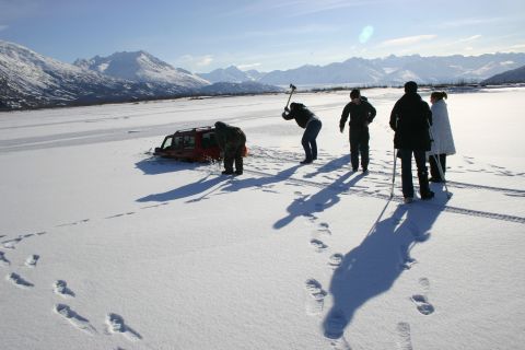 2003 Jeep TJ - People attempt to free a red 2003 Jeep TJ stuck in ice near snowy mountains.