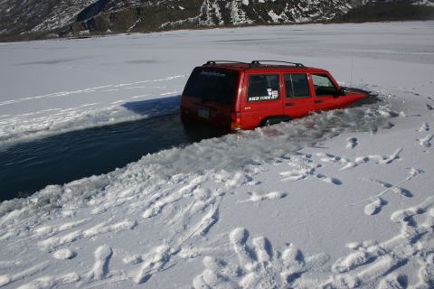 2003 Jeep TJ - Red Jeep Cherokee XJ partially submerged in icy water near a snowy bank.