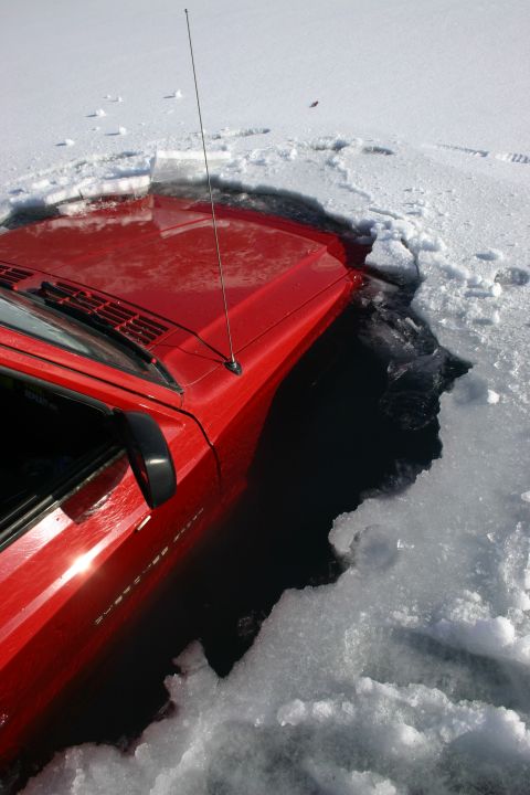 2003 Jeep TJ - A red 2003 Jeep TJ is partially submerged in dark, icy water, with chunks of ice surrounding the vehicle.