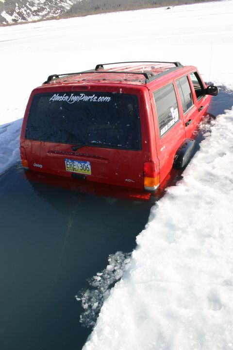 2003 Jeep TJ - A red Jeep Cherokee is partially submerged in dark, icy water with snow on the banks.