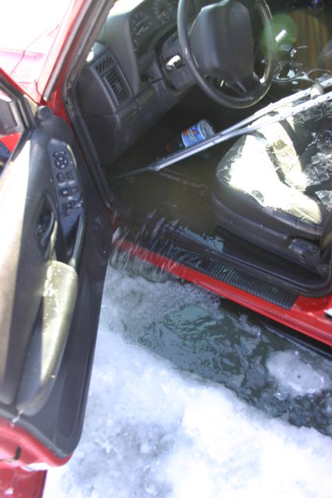 2003 Jeep TJ - Interior of a red Jeep submerged in water and snow, with the driver's door open.