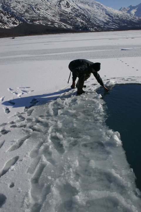 2003 Jeep TJ - A person breaks through the ice on a frozen body of water, with snow-capped mountains visible in the distance under a clear sky.
