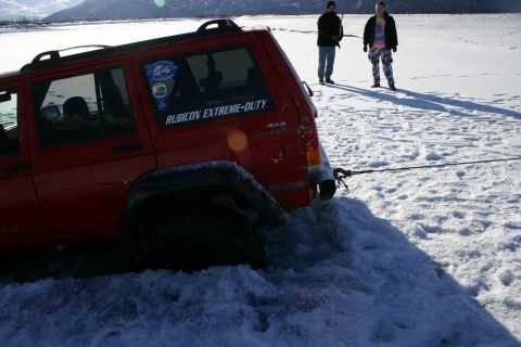 2003 Jeep TJ - A red Jeep Cherokee XJ is stuck in the snow, with two people standing in the background.