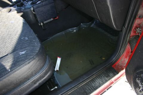 2003 Jeep TJ - Water covers the floor mat inside a red vehicle, with visible damage to the seat upholstery.