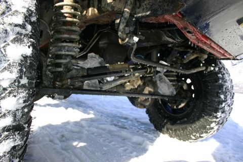 2003 Jeep TJ - The undercarriage and large tires of a vehicle are visible, covered in snow, suggesting off-road use in a cold environment.