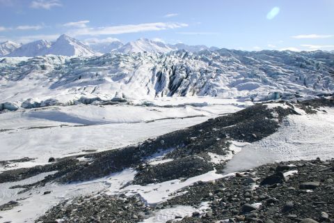 2003 Jeep TJ - A wide expanse of a glacier stretches towards snow-capped mountains under a bright, partly cloudy sky.