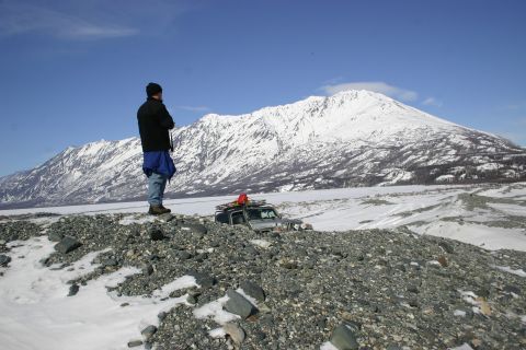 2003 Jeep TJ - A silver Jeep Wrangler navigates a rocky, snow-dusted landscape with a snow-capped mountain range in the background.