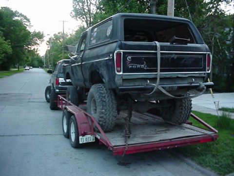 1992 Ford Bronco - A black 1978 Ford Bronco is seen being transported on a trailer, with another vehicle visible behind it on the road.