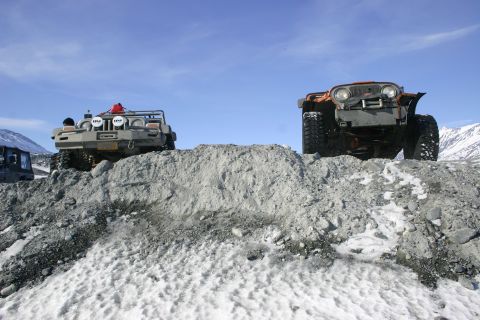 2003 Jeep TJ - Two off-road vehicles navigate a challenging terrain of rocks and snow on a bright, clear day.