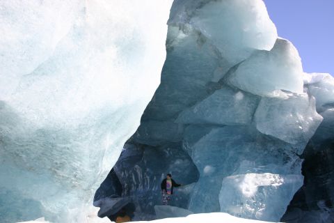2003 Jeep TJ - A person stands within a massive ice cave, surrounded by towering blue ice structures under a clear sky.