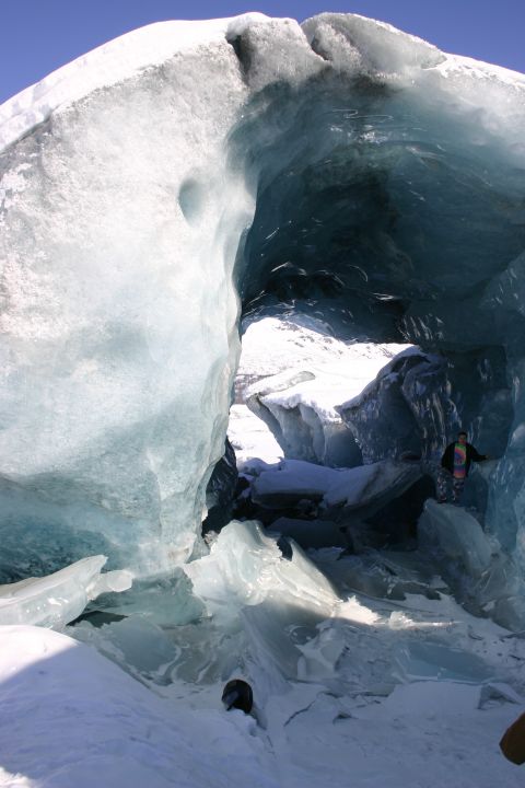 2003 Jeep TJ - People explore the interior of a large ice cave, with sunlight illuminating the blue ice formations.