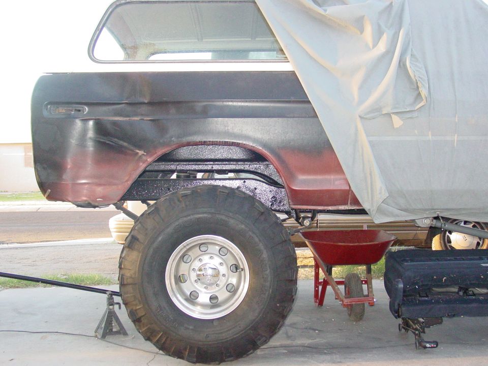 1978 Ford Bronco rear quarter panel with large tire, partially covered by a tarp