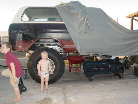 1979 Ford Bronco - Ford Bronco with oversized tires, partially covered, with two children present.