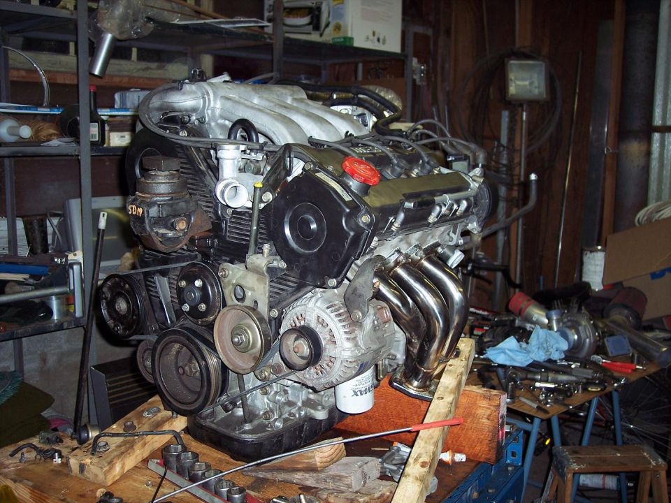 Engine with chrome exhaust headers, on a wooden stand in a workshop