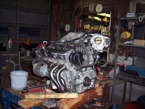 1995 Ford Probe - Engine assembly with chrome headers and intake manifold sits on a workbench in a cluttered garage.