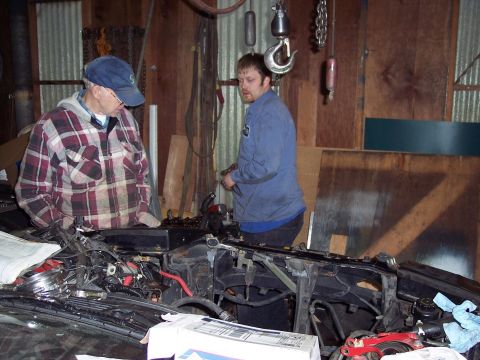 1995 Ford Probe - Two men are gathered around the engine compartment of a car in a workshop.