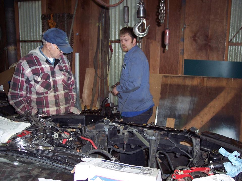 Two guys looking at an open car engine bay in a garage