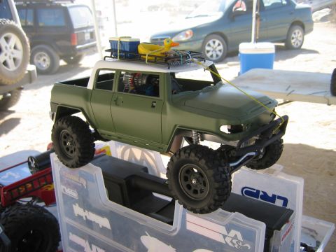 1985 Ford Bronco - A remote-controlled rock crawler truck is displayed outdoors, with other vehicles and a cooler in the background.