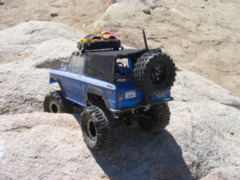 1985 Ford Bronco - RC rock crawler truck with spare tire on back, driving on rocks.
