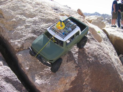 1985 Ford Bronco - An off-road vehicle, equipped with a roof rack carrying gear, tackles a challenging rocky obstacle course.