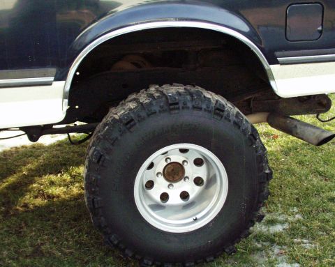1989 Ford Bronco - Close-up of the rear wheel and fender of a Ford Bronco, showing its off-road tires and two-tone paint scheme.