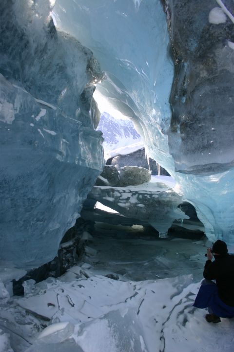 2003 Jeep TJ - A person photographs the view from within a glacial ice cave, surrounded by blue ice formations and snow.