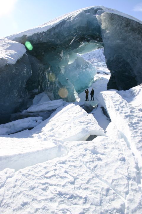 2003 Jeep TJ - Explorers stand within a glacial ice cave, dwarfed by the immense blue ice formations and surrounding snow.