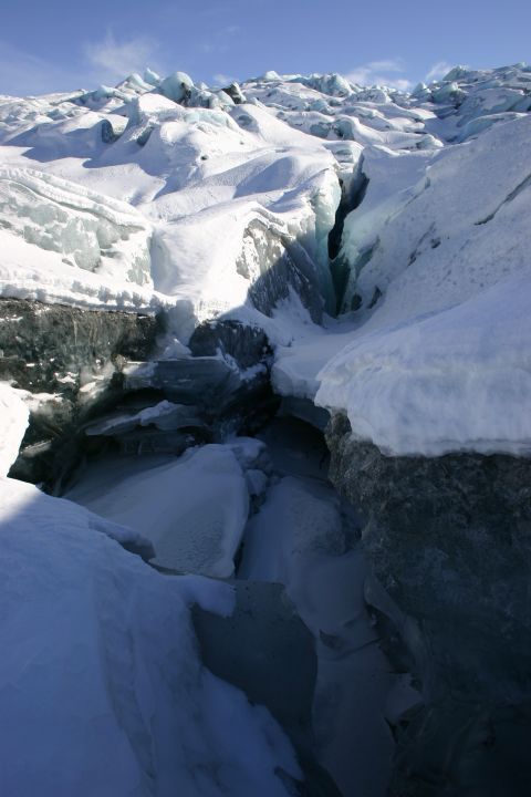 2003 Jeep TJ - A deep crevasse cuts through a snow-covered glacier, revealing blue ice formations within its depths under a clear sky.