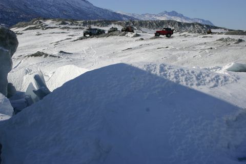 2003 Jeep TJ - Several off-road vehicles traverse a snowy, mountainous area under a clear blue sky.