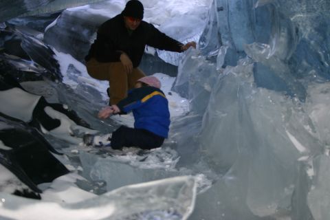 2003 Jeep TJ - Two individuals navigate the icy terrain within a striking blue ice cave, surrounded by snow and ice formations.