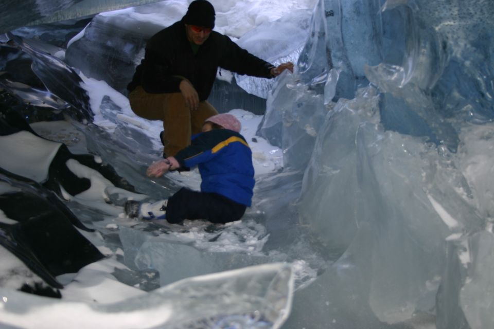 Two people exploring a blue ice cave with snow