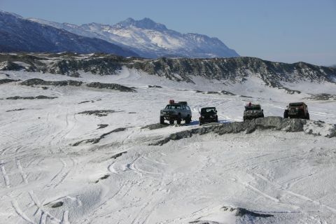 2003 Jeep TJ - A group of SUVs traverse a snow-covered, rocky landscape under a clear sky, with a mountain range in the distance.