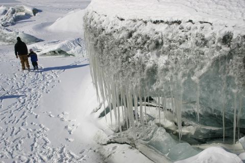 2003 Jeep TJ - Two people walk through a snowy landscape dotted with footprints, near large ice formations and icicles.